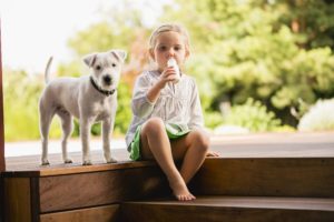 Young girl sitting on wooden steps with dog eating doughnut Otoczenie do potrzeb dzieci – Dom z myślą o najmłodszych